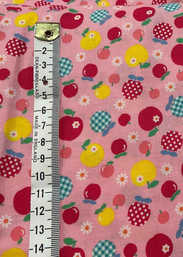 Fabric with apple pattern on a pink background, measured with a ruler.