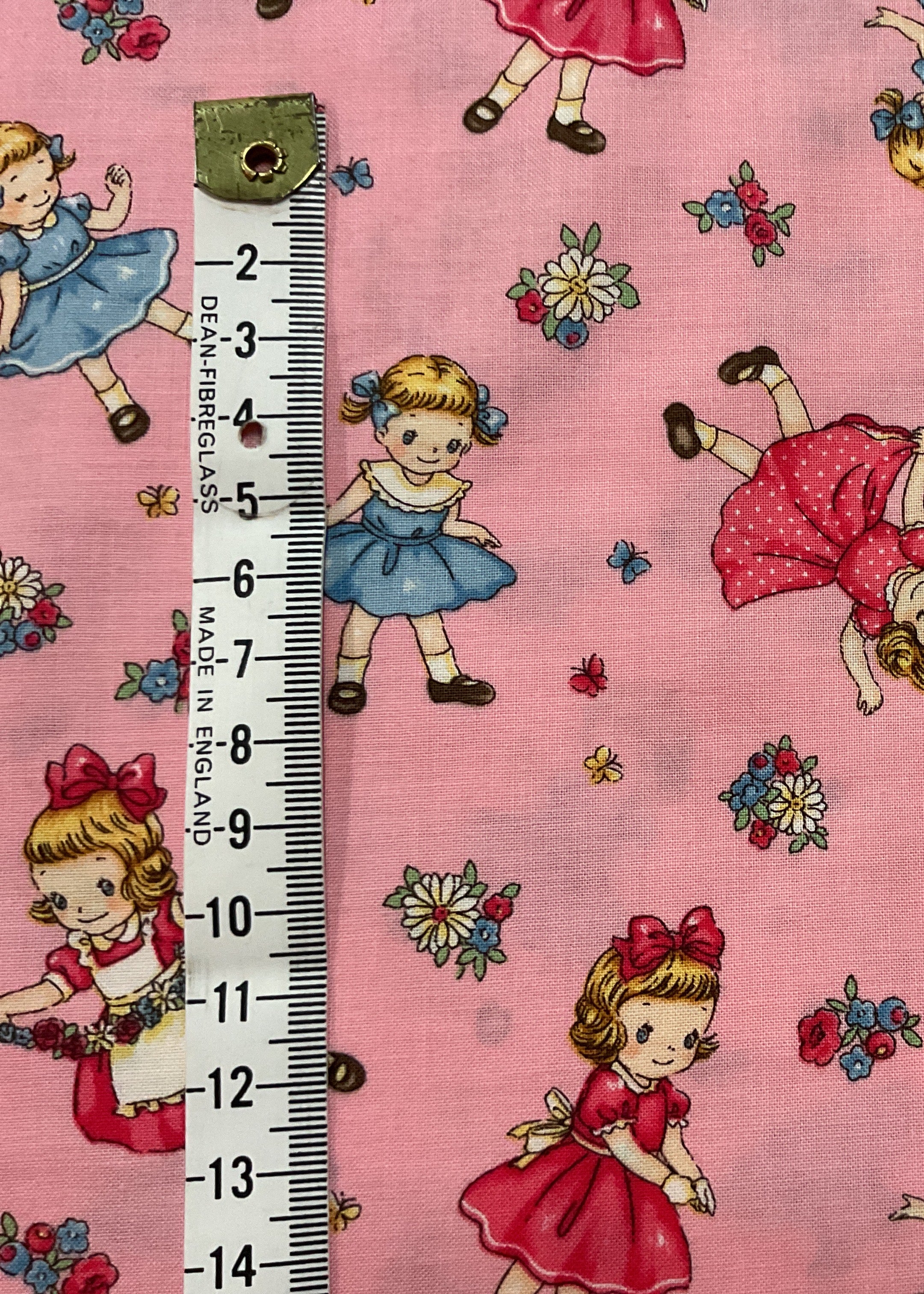 Fabric with vintage-style girl illustrations on a pink background, featuring a ruler for scale.