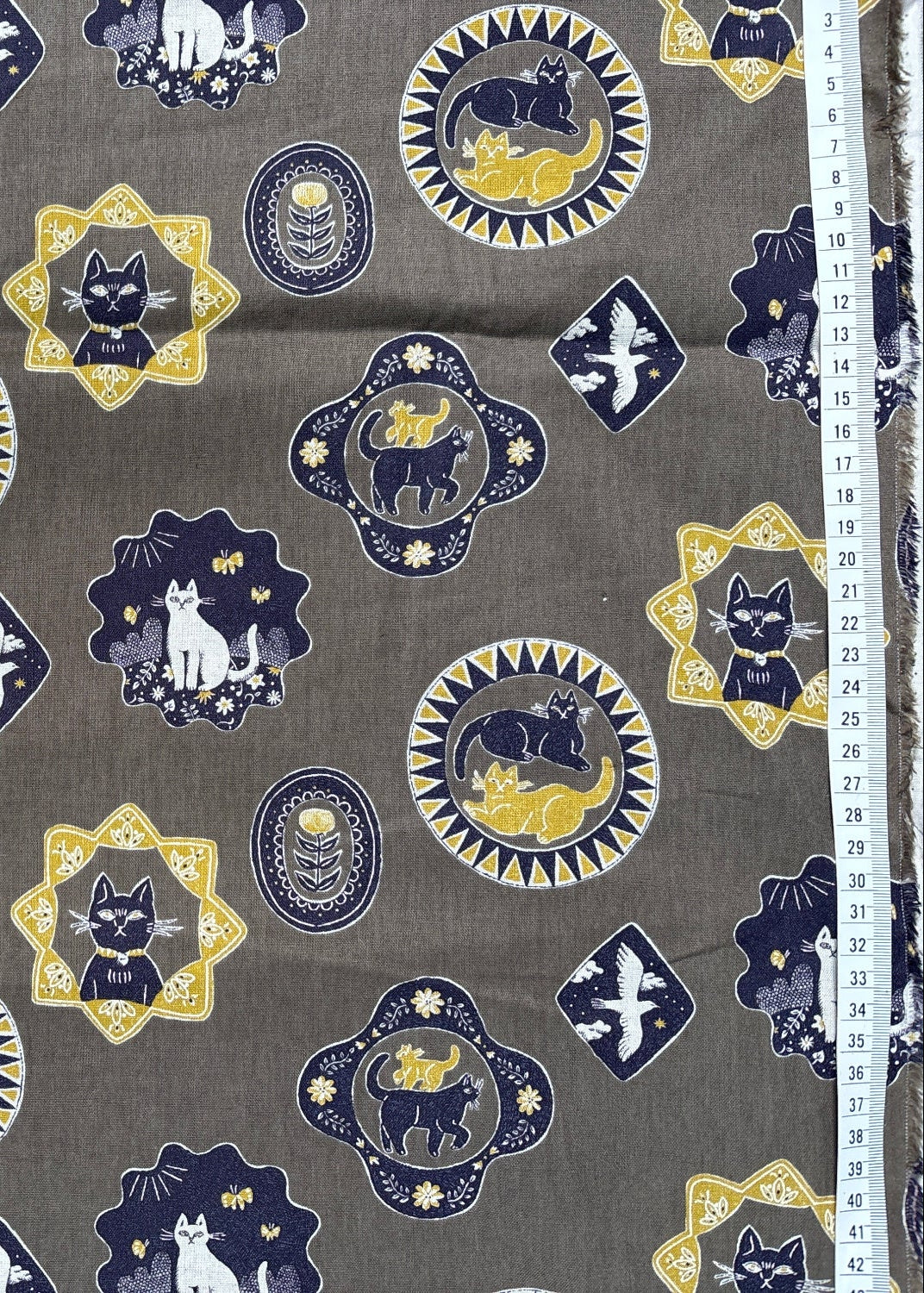 Patterned fabric with cat designs on a gray background, measured by a ruler.