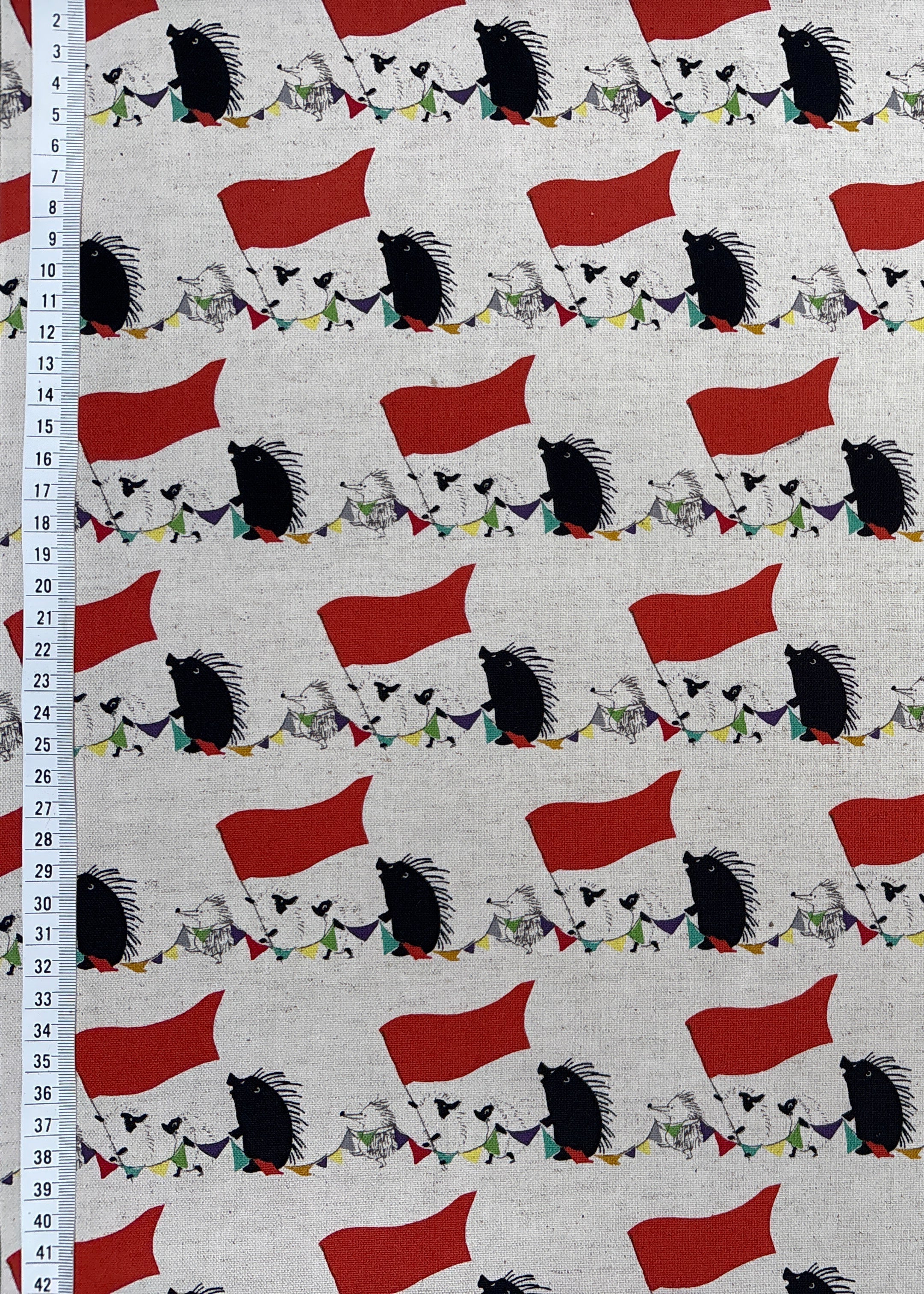 Fabric with a pattern of red flags and black and white shapes on a white background, with a ruler for scale.