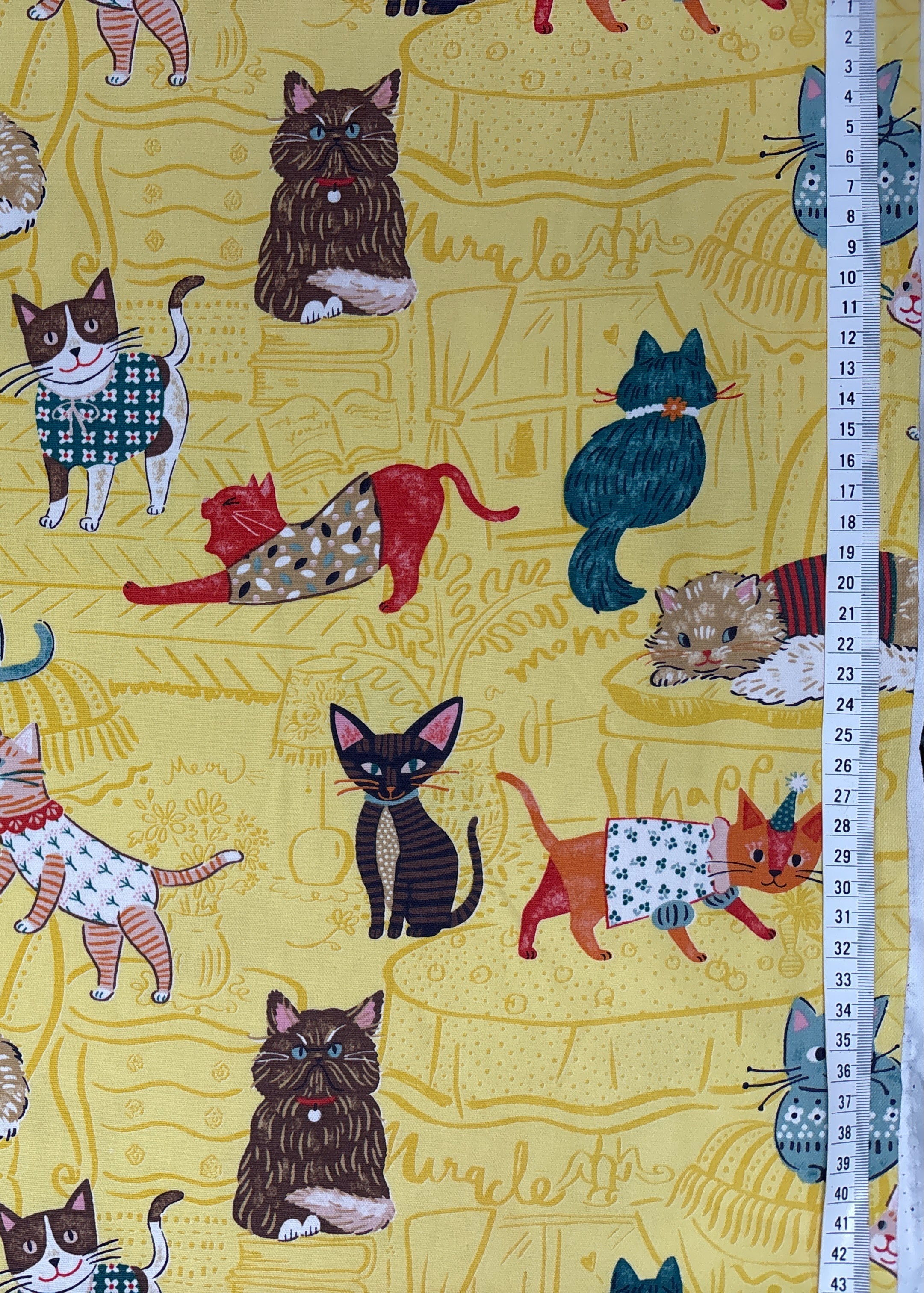 Patterned fabric with cartoon cats on a yellow background, accompanied by a ruler for scale.
