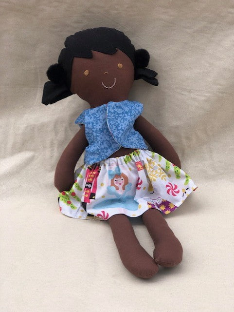 Handmade doll with a blue top and colorful skirt on a beige background